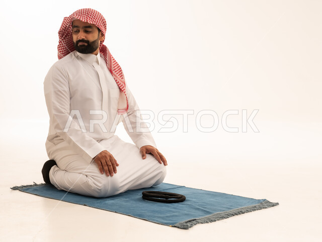 رجل سعودي يؤدي الصلاة على سجادة خلفية بيضاء