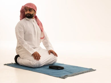 رجل سعودي يؤدي الصلاة على سجادة خلفية بيضاء
