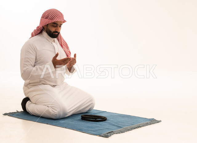 رجل سعودي يصلي على السجادة بخلفية بيضاء