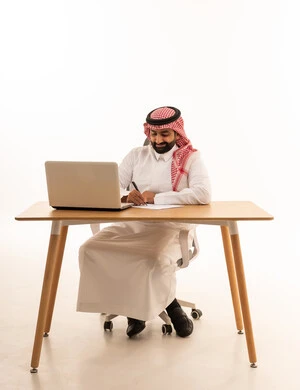 Saudi Businessman Writing at Office Desk with Laptop