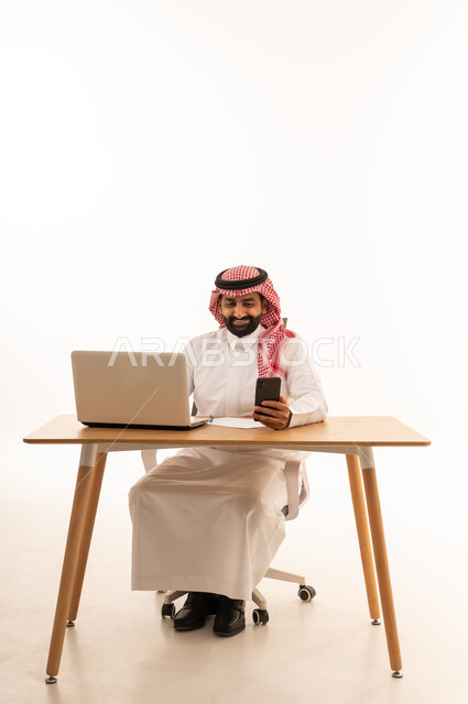 رجل أعمال سعودي يعمل على لابتوب وهاتف ذكي