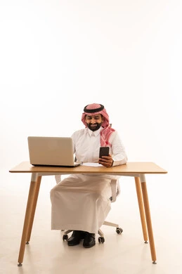 Saudi Businessman Working on Laptop with Smartphone