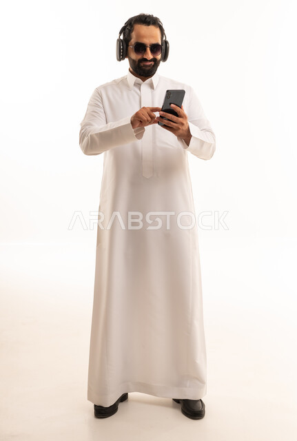 رجل سعودي بالثوب يستخدم الجوال مع سماعات