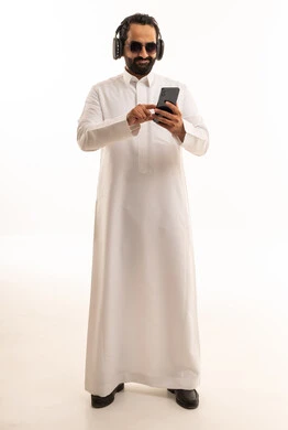 رجل سعودي بالثوب يستخدم الجوال مع سماعات