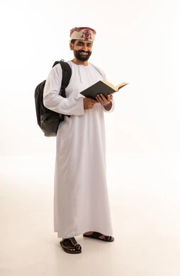 طالب عُماني يرتدي الدشداشة ويحمل حقيبة وكتاباً