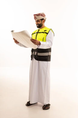 مهندس عماني يرتدي سترة السلامة يراجع مخططات هندسية