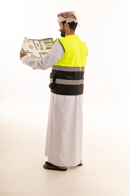 مهندس عماني يرتدي سترة السلامة ويقرأ مخططاً هندسياً