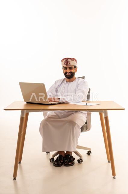 رجل أعمال عماني يعمل على الحاسوب المحمول بخلفية بيضاء