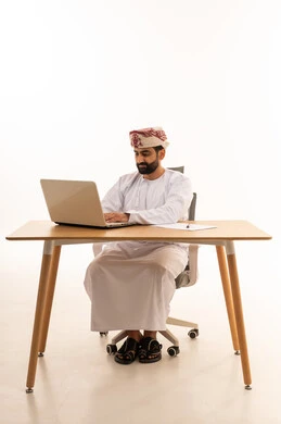 Omani Man Working on Laptop at White Desk