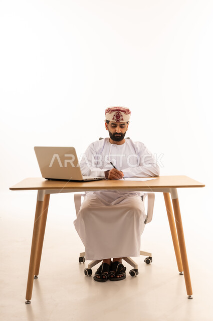رجل عُماني يعمل على مكتب مع جهاز لابتوب
