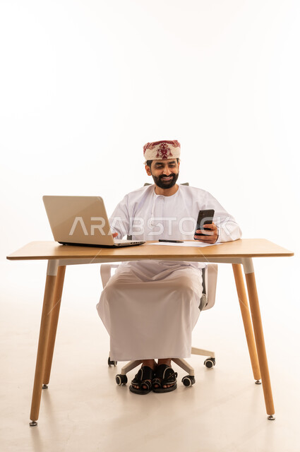 Omani Man Working on Laptop and Smartphone at Desk
