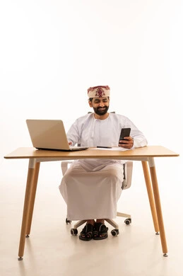 رجل عماني يعمل على المحمول والهاتف الذكي في المكتب