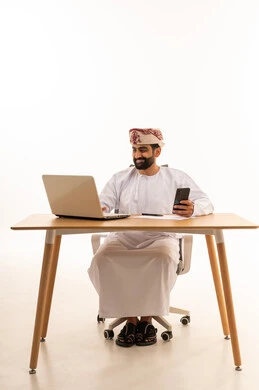 رجل أعمال عماني يستخدم الحاسوب والهاتف على المكتب