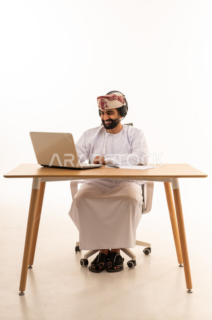 رجل عُماني يعمل على كمبيوتر محمول بسماعة رأس