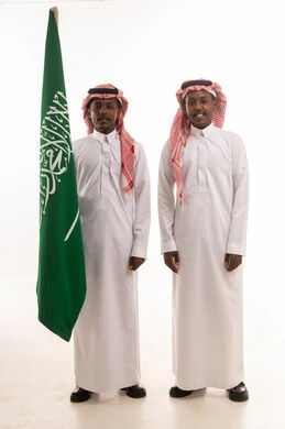 رجلان سعوديان يحملان علم السعودية بالزي الرسمي