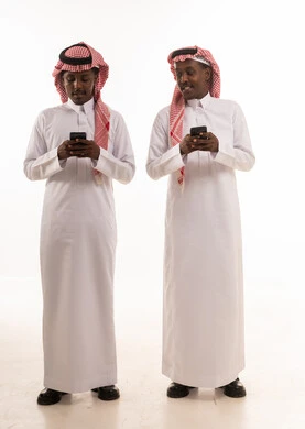 رجال سعوديون بالثوب التقليدي يستخدمون الهواتف الذكية
