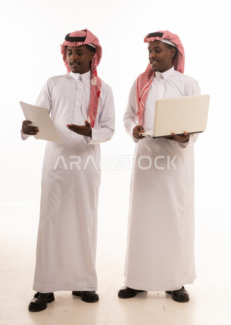 رجال سعوديون يعملون على كمبيوتر محمول ومستندات