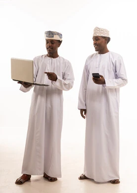 رجال عمانيون يستخدمون الحاسوب المحمول والهاتف الذكي