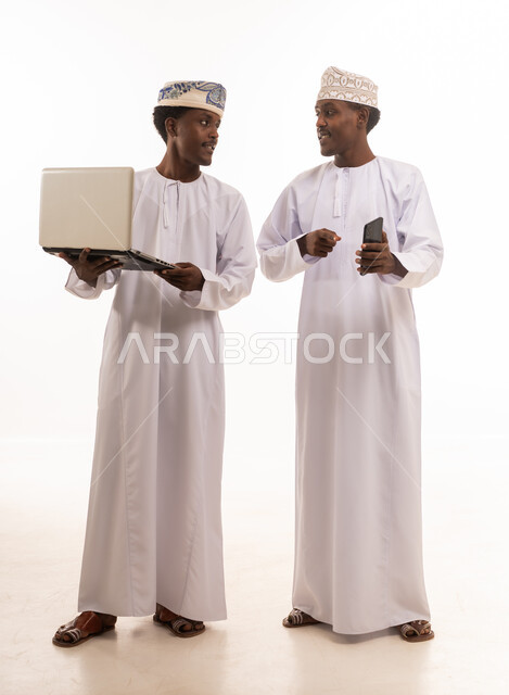رجلان عمانيان يستخدمان الحاسوب المحمول والهاتف الذكي