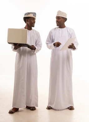 رجال عمانيون بالزي التقليدي مع كمبيوتر محمول ومستند