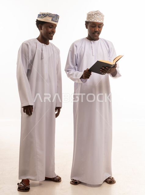 رجال عمانيون يقرأون كتاباً بالزي التقليدي بخلفية بيضاء