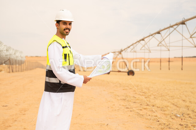 مهندس سعودي مع مخططات هندسية في موقع ري صحراوي