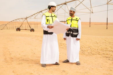 مهندسون عُمانيون مع مخططات في حقل زراعي صحراوي