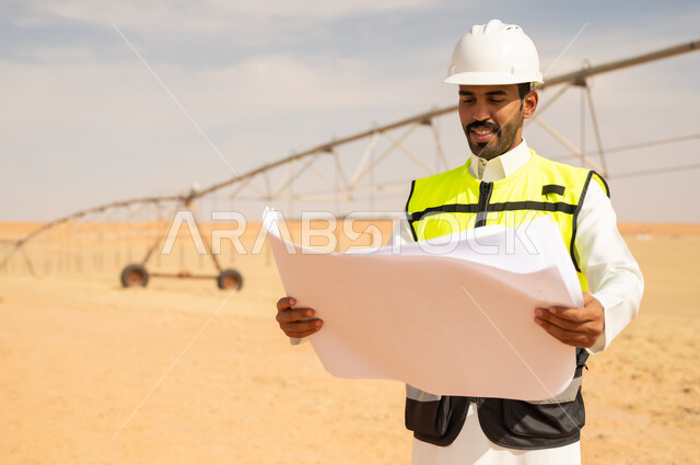 مهندس سعودي يراجع مخططات في موقع إنشائي صحراوي