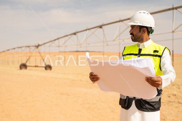 مهندس سعودي يحمل مخططات في موقع زراعي صحراوي