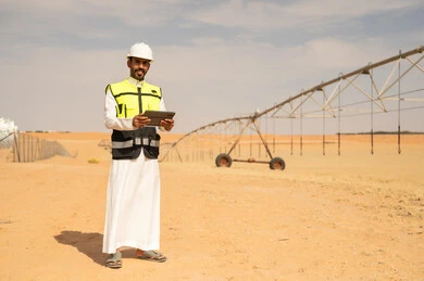 مهندس سعودي مع جهاز لوحي في مزرعة صحراوية