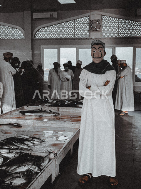 A picture of an Omani man wearing a mask inside the fish market in the Sultanate of Oman, a shop selling fresh fish