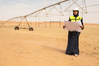 مهندسة سعودية في حقل زراعي صحراوي مع مخططات