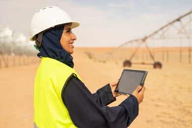 مهندسة سعودية مع جهاز لوحي في مزرعة صحراوية