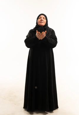 امرأة عربية مسنة ترتدي عباءة سوداء تدعو في الاستوديو