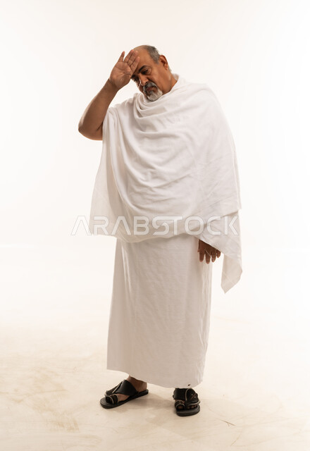 رجل عربي مسن بملابس الإحرام يمسح العرق