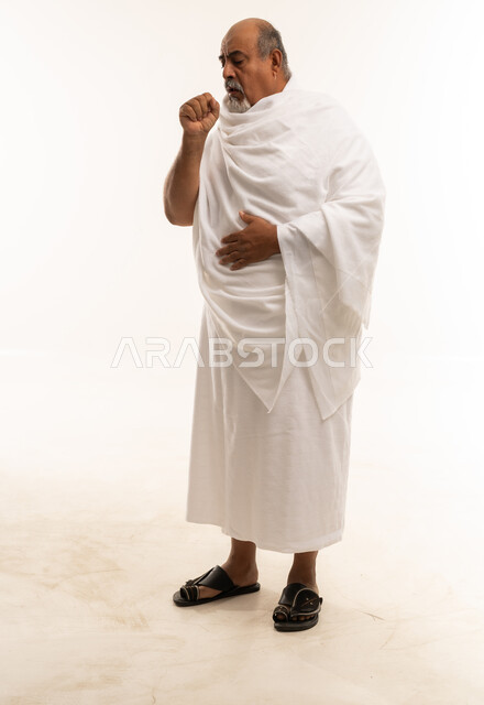 رجل سعودي مسن بملابس الإحرام يسعل أمام خلفية بيضاء