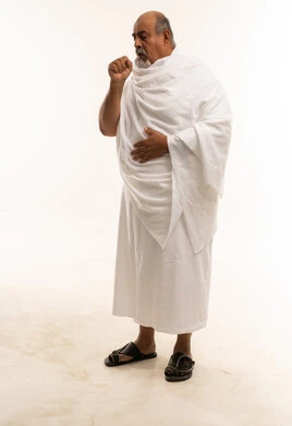 رجل سعودي مسن بملابس الإحرام يسعل أمام خلفية بيضاء