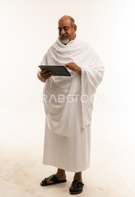 رجل سعودي بملابس الإحرام يستخدم تابلت بخلفية بيضاء