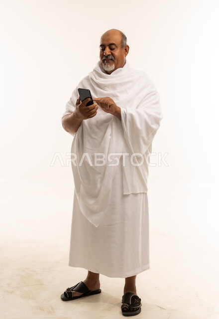 رجل سعودي مسن بملابس الإحرام يستخدم الجوال