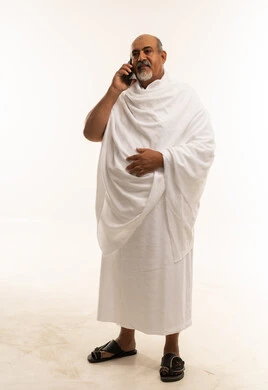 رجل سعودي مسن بملابس الإحرام يتحدث بالهاتف الذكي