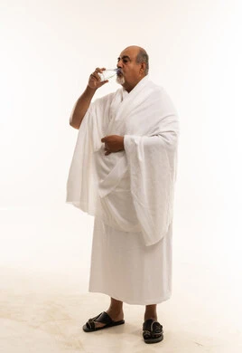 رجل عربي بملابس الإحرام يشرب الماء في استوديو