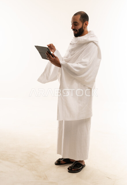 رجل سعودي بملابس الإحرام يحمل جهاز لوحي