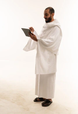 رجل سعودي بملابس الإحرام يحمل جهاز لوحي