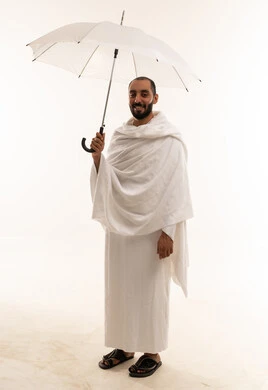رجل سعودي بملابس الإحرام يحمل مظلة بيضاء