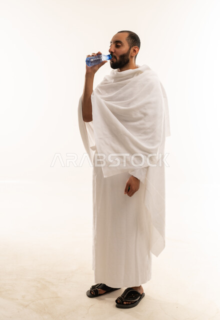 رجل سعودي بملابس الإحرام يشرب الماء خلفية بيضاء