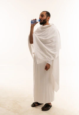 رجل سعودي بملابس الإحرام يشرب الماء خلفية بيضاء