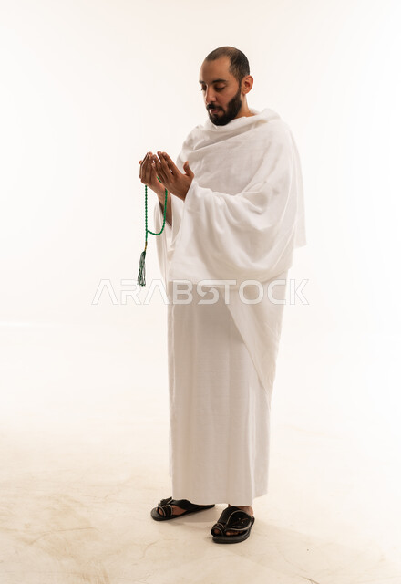 رجل مسلم بملابس الإحرام يدعو ويحمل سبحة
