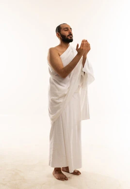 رجل سعودي بملابس الإحرام يدعو على خلفية بيضاء