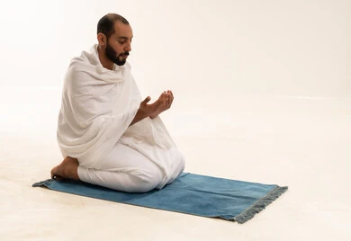 رجل عربي بملابس الإحرام يدعو على سجادة صلاة