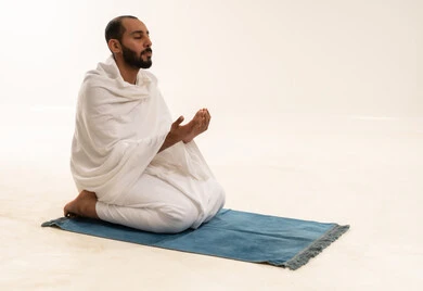 رجل بملابس الإحرام يدعو على سجادة الصلاة